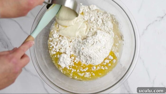 adding sourdough starter to a glass bowl with flour and butter.