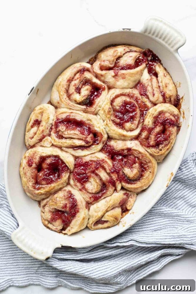 overhead photo of sourdough strawberry rolls in a oval baking dish on a marble countertop with a blue and white stripped towel
