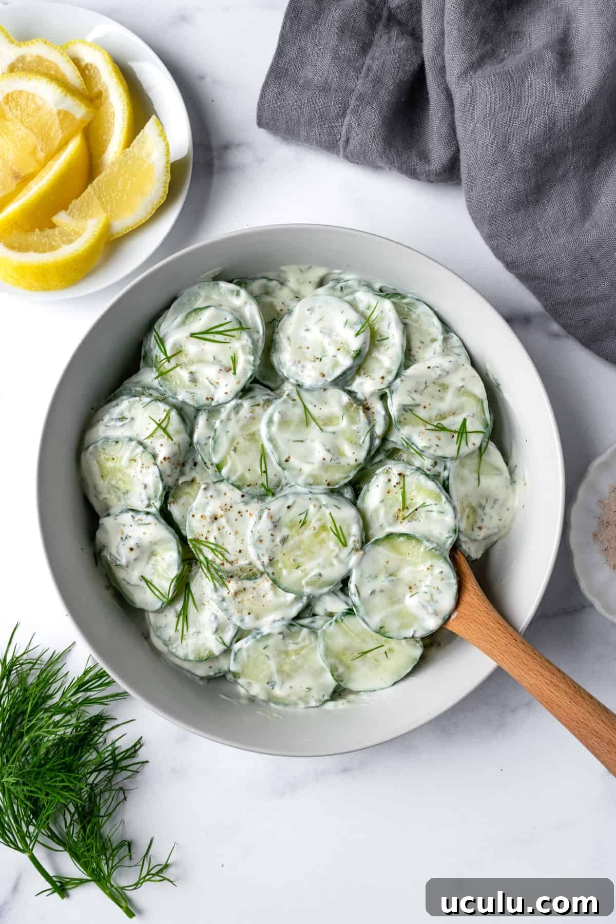 Greek Yogurt Cucumber Salad in a white bowl with a wooden serving spoon.