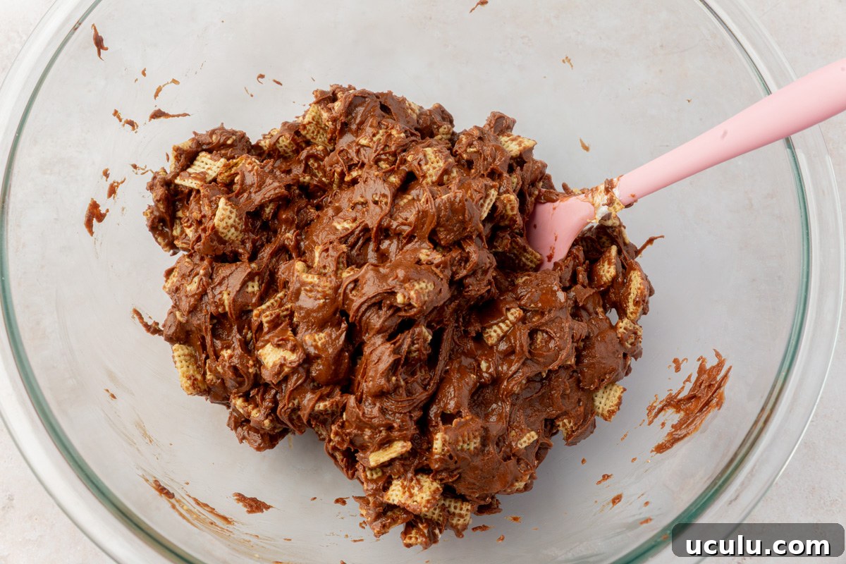 Chocolate-coated cereal mixture fully combined and clumped together in a glass bowl with a pink spatula.