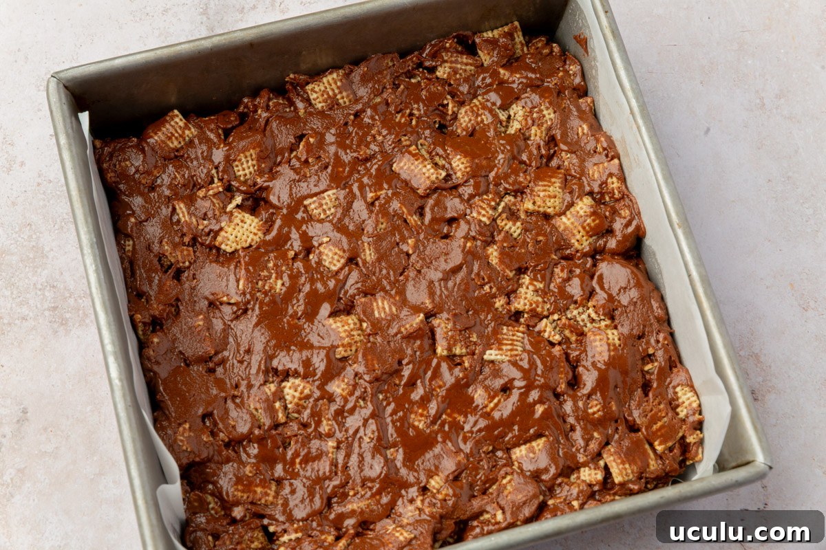 Chocolate cereal mixture evenly pressed into a square baking pan lined with parchment paper.