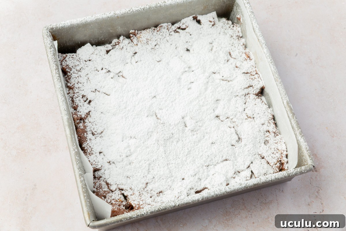A pan of puppy chow bars fully set and generously dusted with powdered sugar.