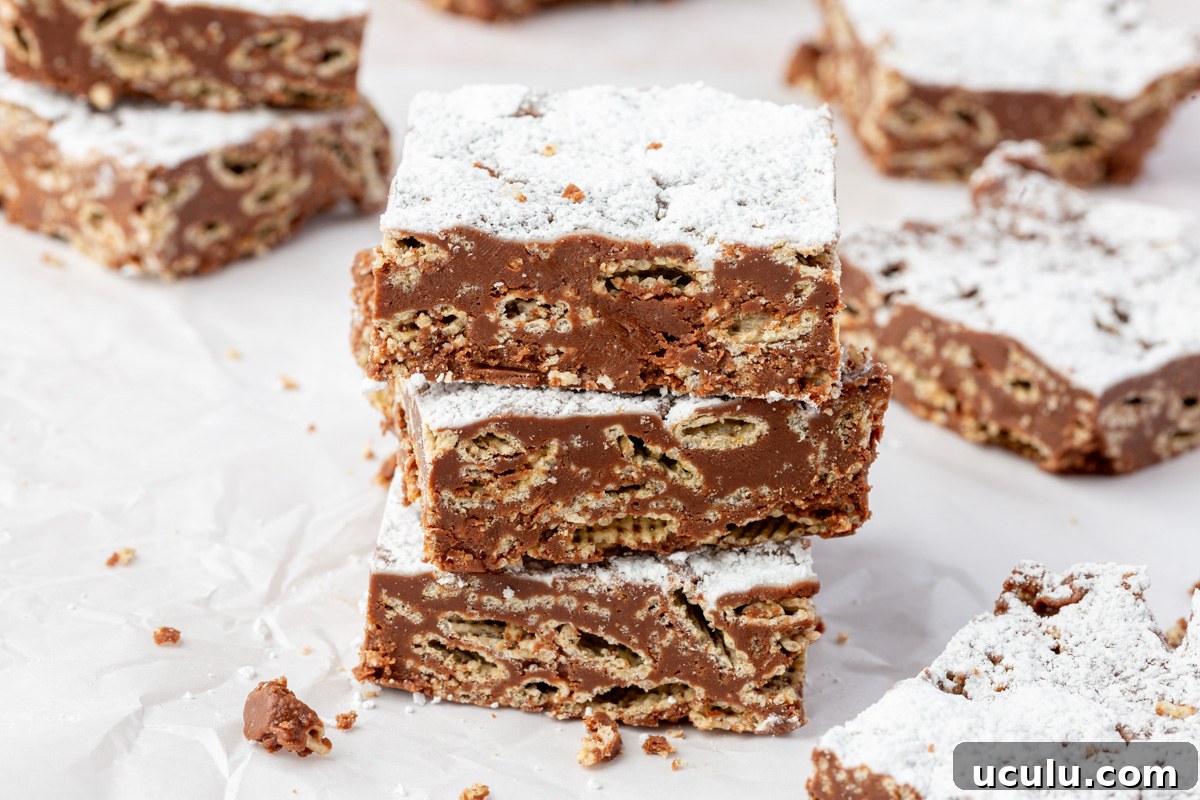 Three puppy chow bars stacked on parchment paper, with powdered sugar dusted on top and cereal pieces visible in the chocolate layer.
