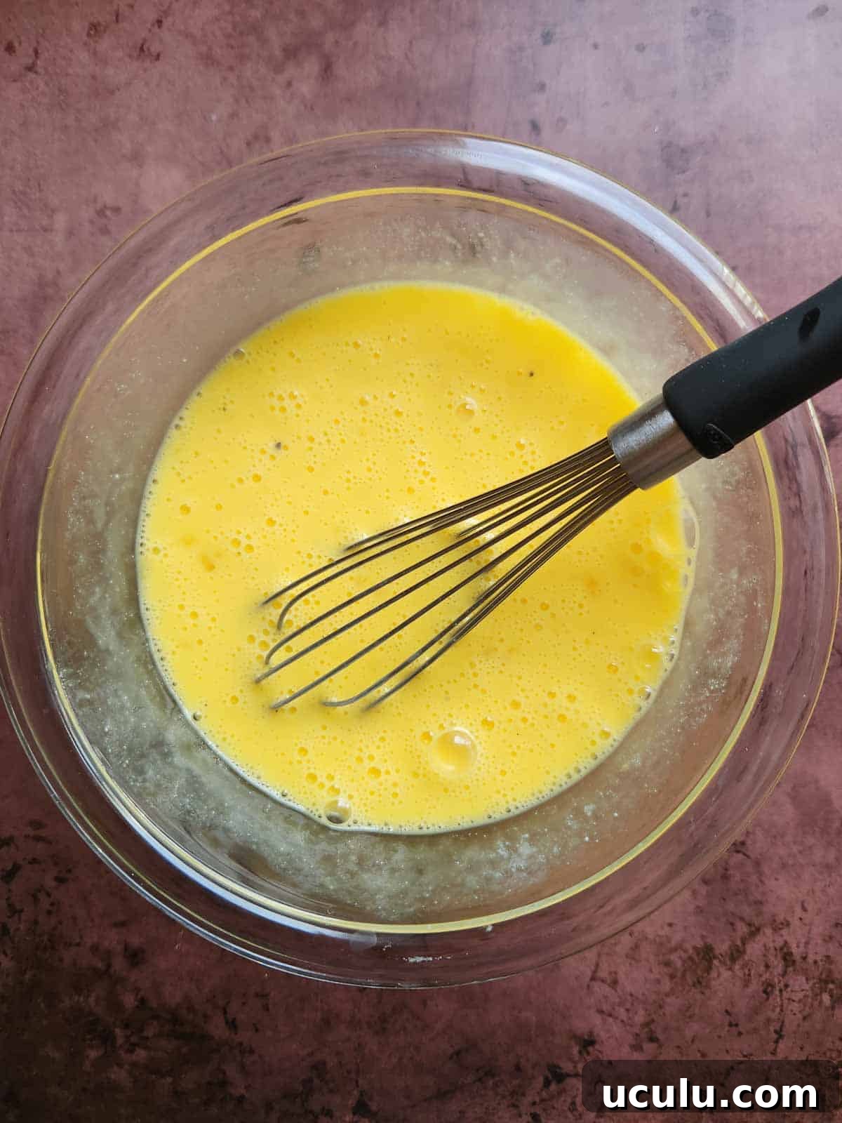 Scrambled egg mixture in a clear bowl with a whisk.