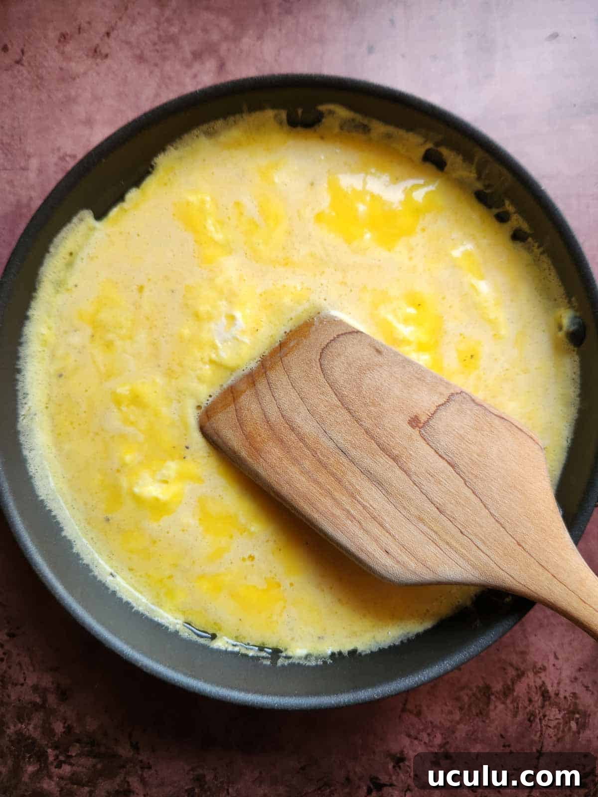 Scrambled eggs in a pan with a wooden spoon.