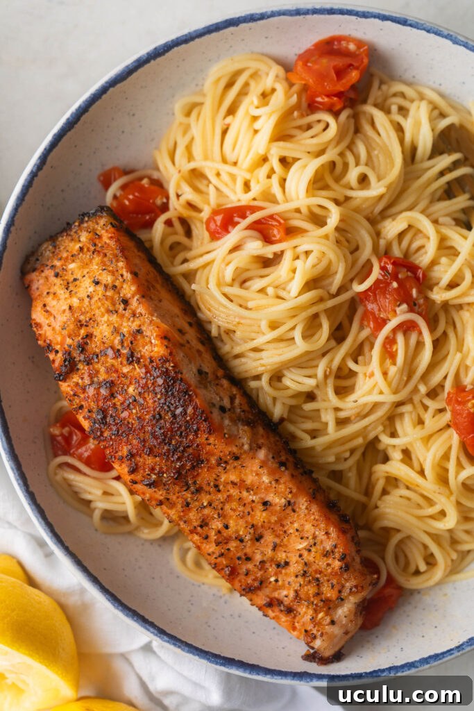 Bowl of Angel hair pasta with garlic butter scampi sauce with cherry tomatoes and a piece of cooked salmon.