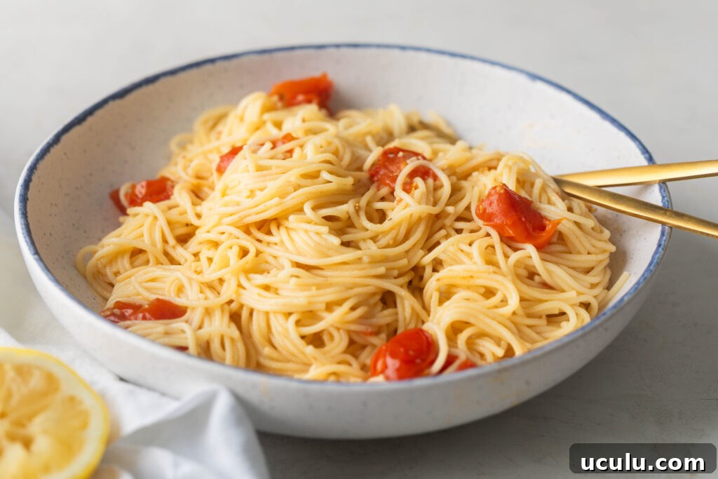 Bowl of Angel Hair pasta with cherry tomatoes and garlic butter scampi sauce with a gold fork and spoon.