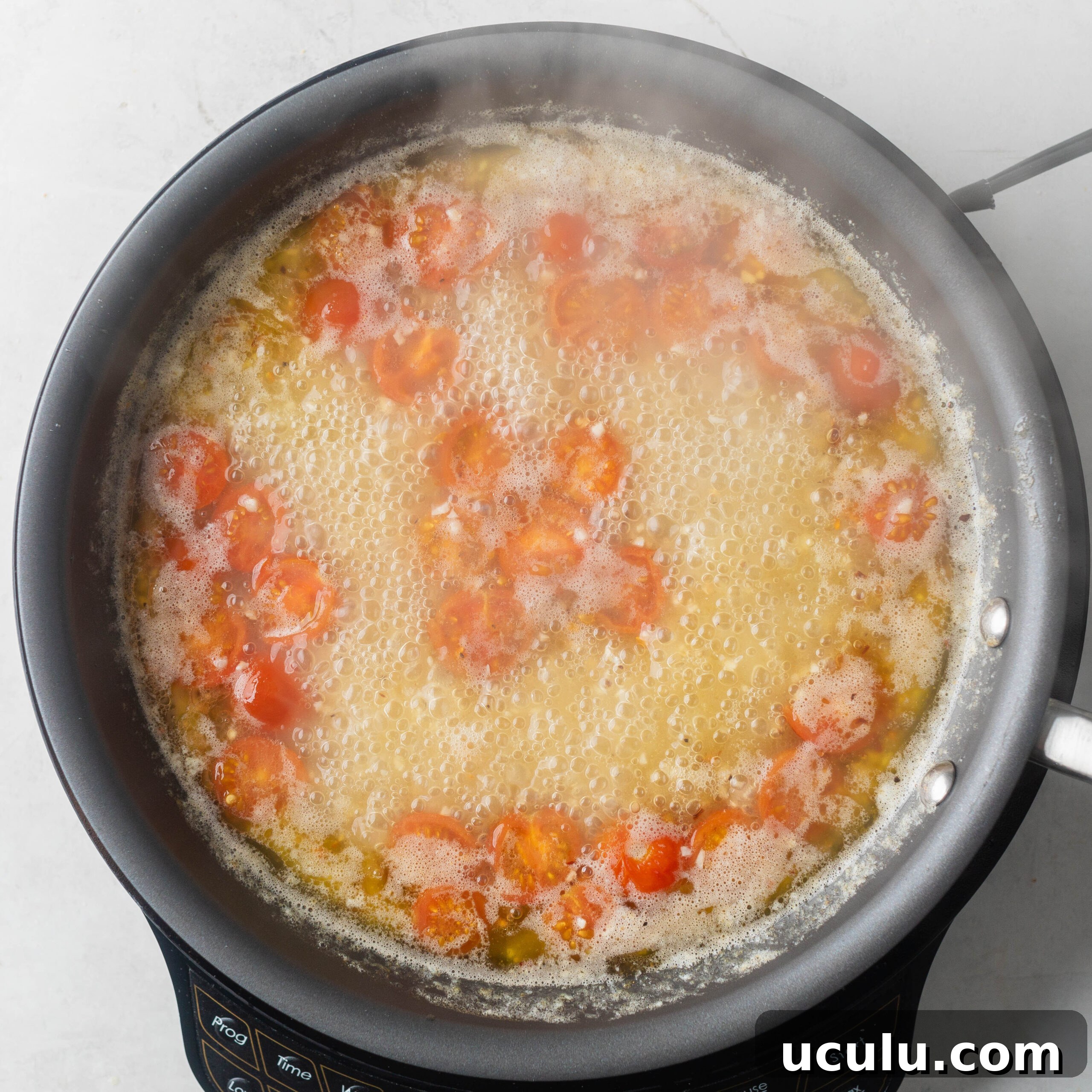 Adding cherry tomatoes, chicken stock and spices to sautéed garlic.