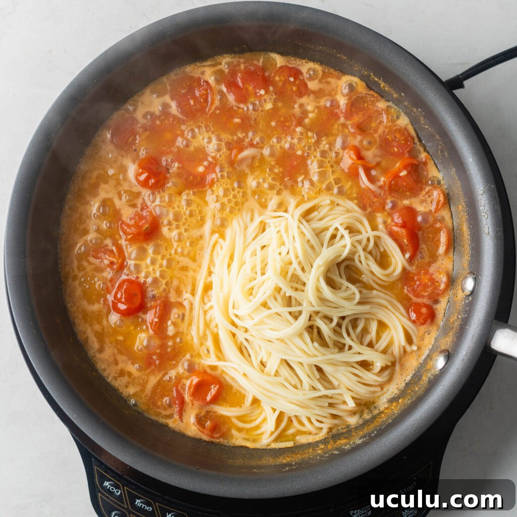Adding cooked pasta to reduced scampi sauce.
