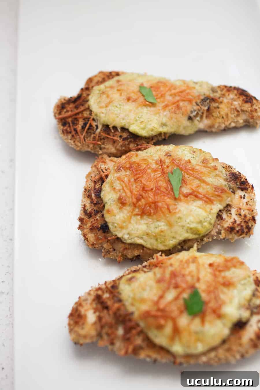 Three Cheesy Ranch Parmesan chicken breasts served on a white plate.