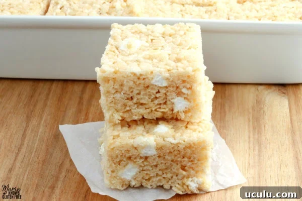 two gluten-free rice krispies treats stacked on top of each other with the pan of treats in the background