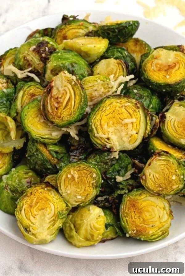 Bright green and crispy brussel sprouts on a white plate sprinkled with parmesan cheese