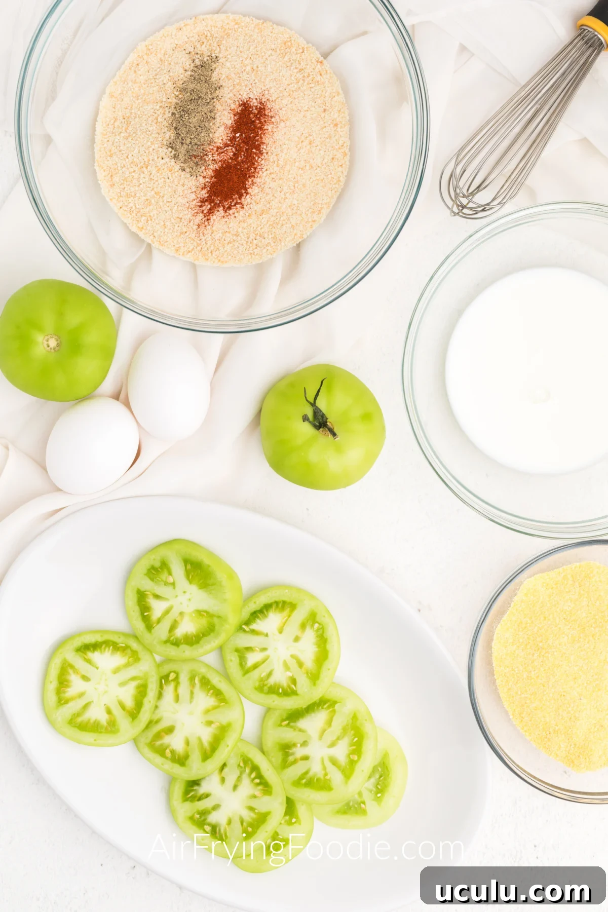 Sliced green tomatoes on a white plate with ingredients surrounding them on a table.