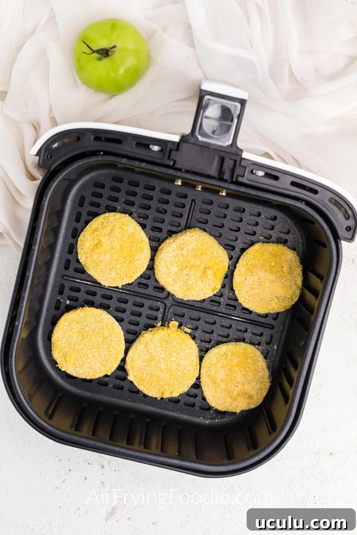 Coated green tomatoes in air fryer basket ready to be cooked.