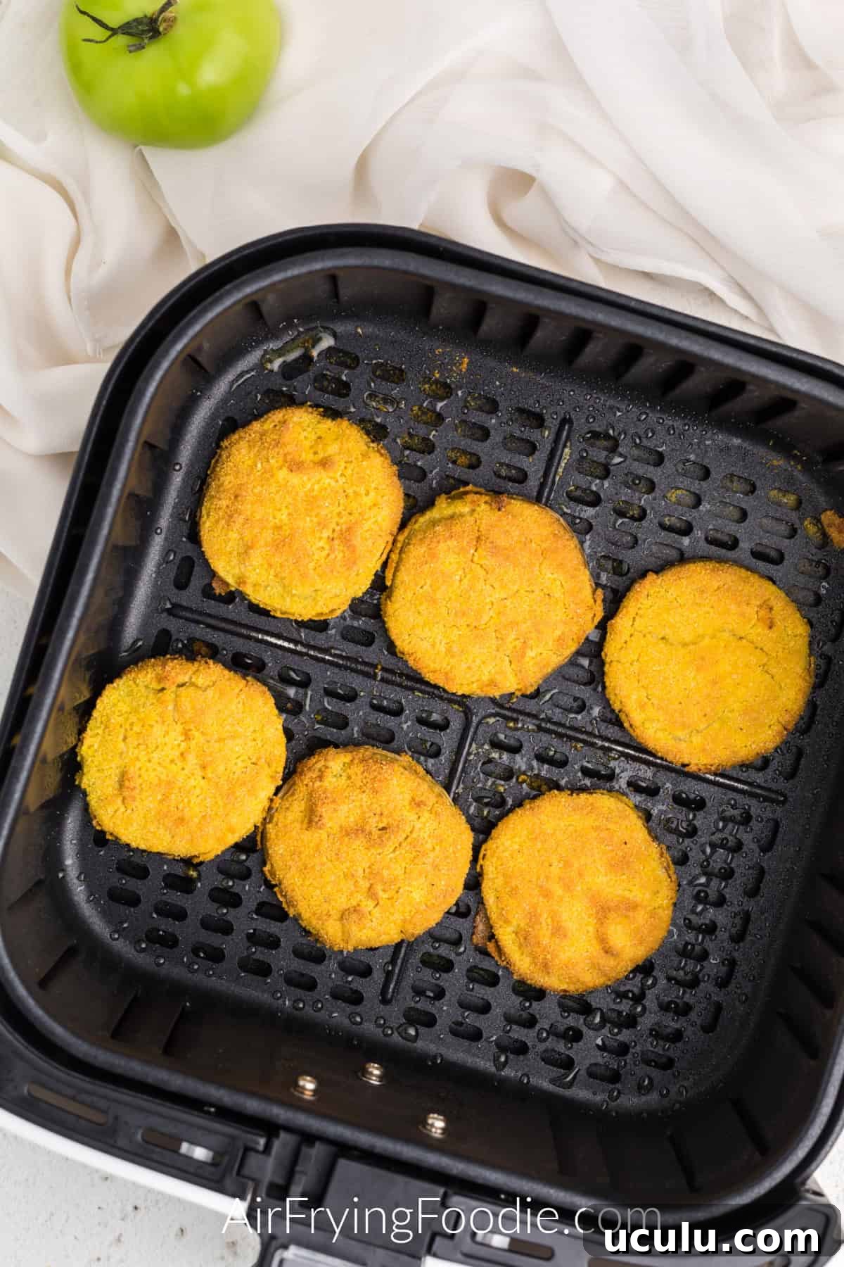 Air Fryer Fried Green Tomatoes in the basket of the air fryer, fully cooked and golden brown.