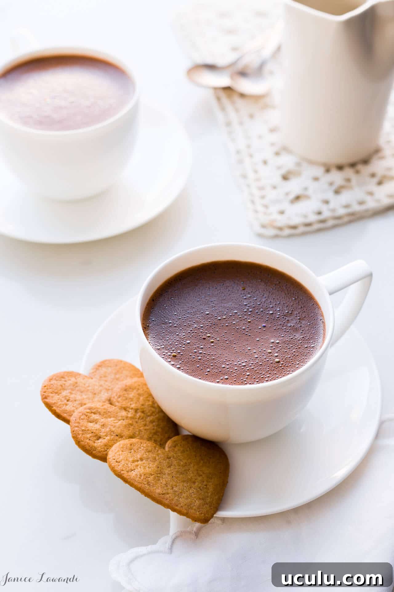 Homemade hot chocolate served in white cups, white saucers, and heart-shaped cookies.