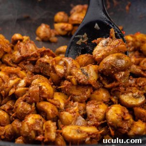 Indian Mushroom Bhaji Recipe | Flavorful Mushroom Curry Guide 12 Stirring mushroom bhaji curry with a black cooking in a pan
