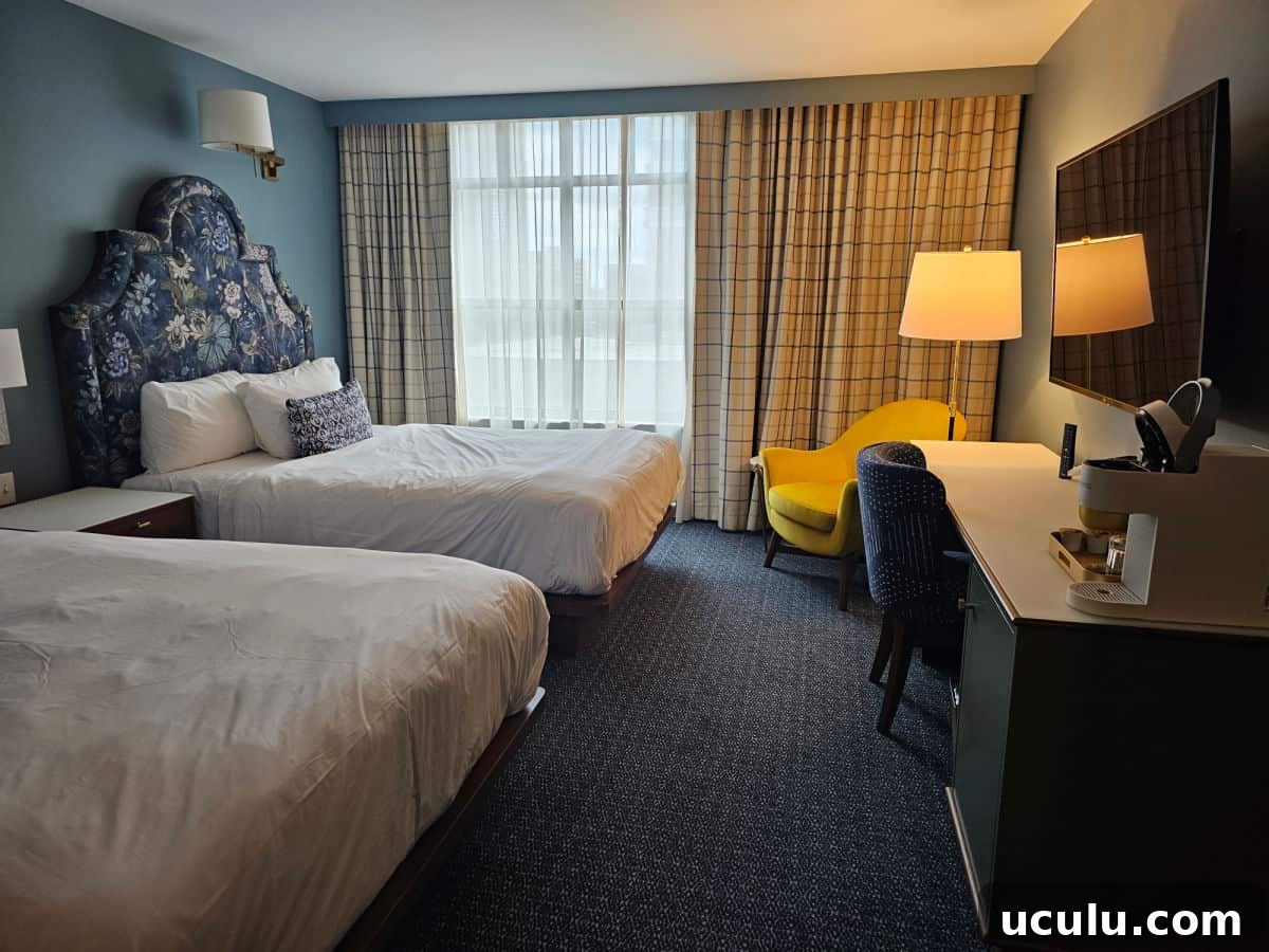 The Bradley Hotel in Fort Wayne, Indiana — Historic Tour Video 4 two wueen beds, yellow chair next to a lamp, and work desk in Bradley hotel room