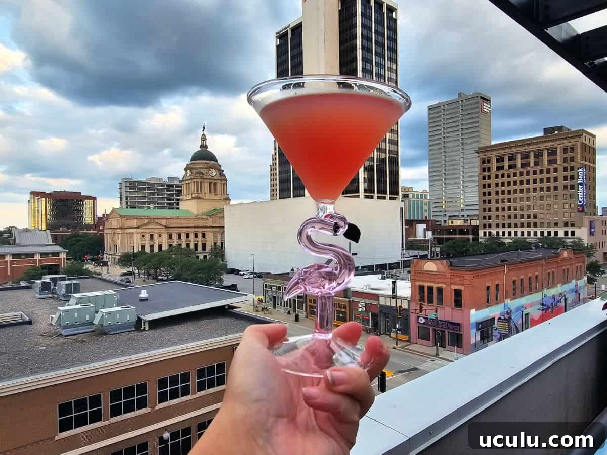 The Bradley Hotel in Fort Wayne, Indiana — Historic Tour Video 10 Hand holding a pink drink in a flamingo glass with the Fort Wayne skyline in the background