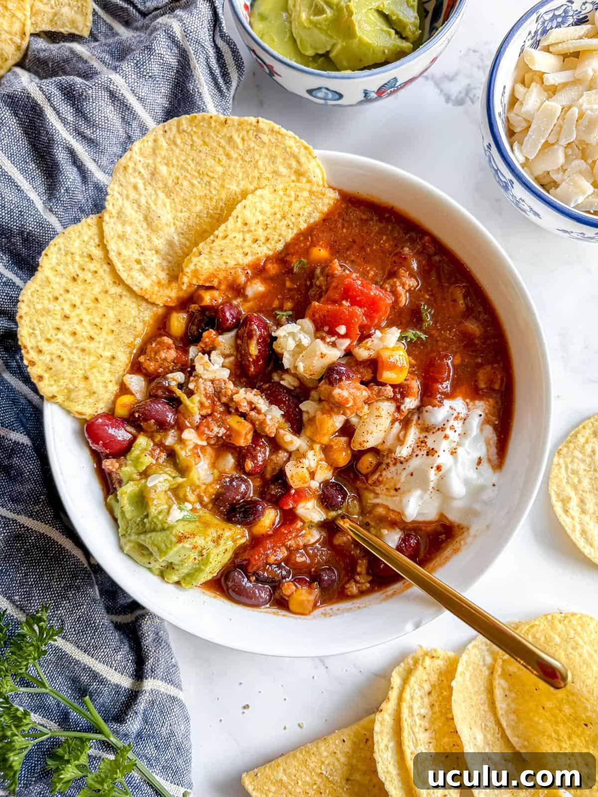 Healthy turkey chili in a bowl with a spoon mixing all the toppings in it.