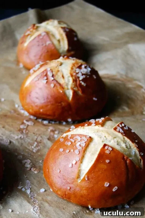 Three pretzel rolls on a sheet of parchment sprinkled with coarse salt.