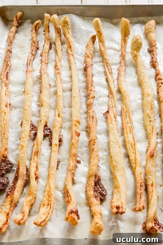 A baking sheet lined with parchment filled with 10 long, thin crispy cheese sticks.