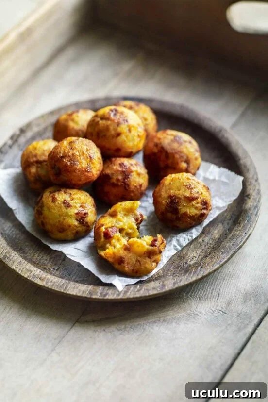 A wooden bowl filled with golf-ball-size fried potato and chouriço balls on a wooden tray.