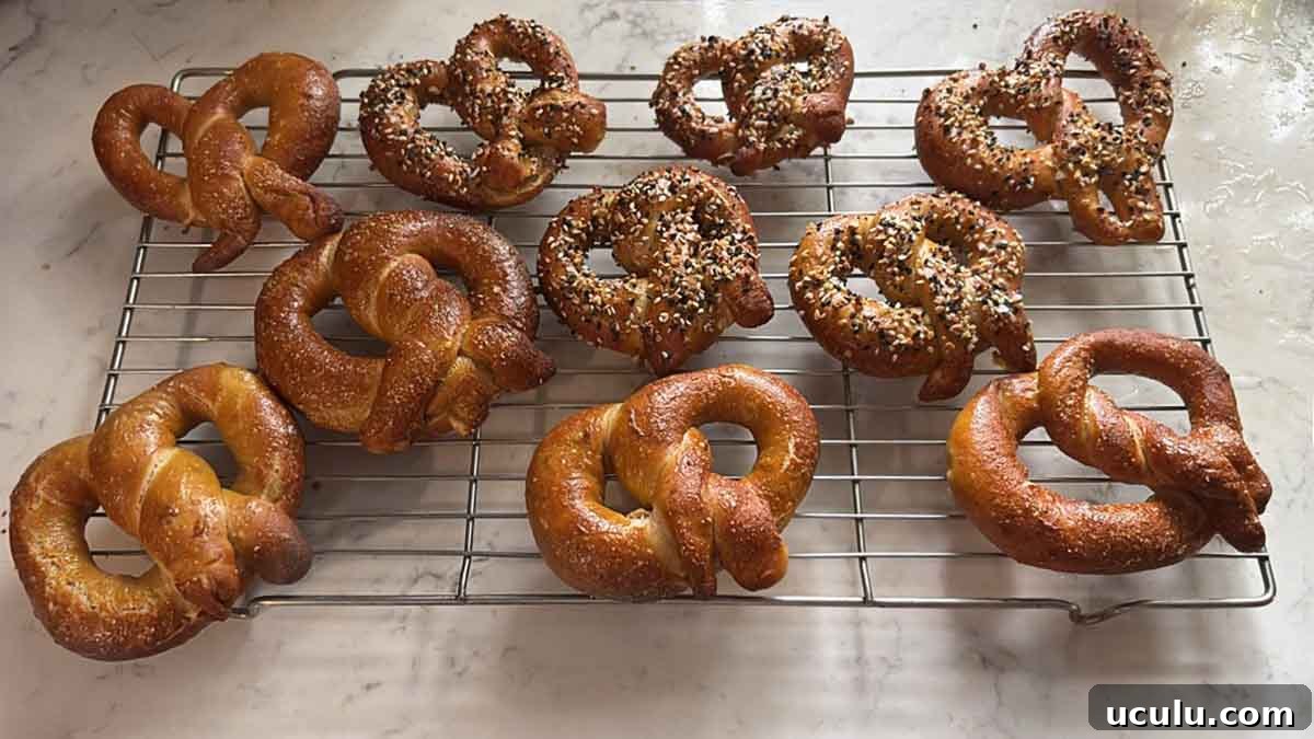 Ten homemade soft pretzels, half plain the other half coated with white and black sesame seeds cooling on a wire rack.
